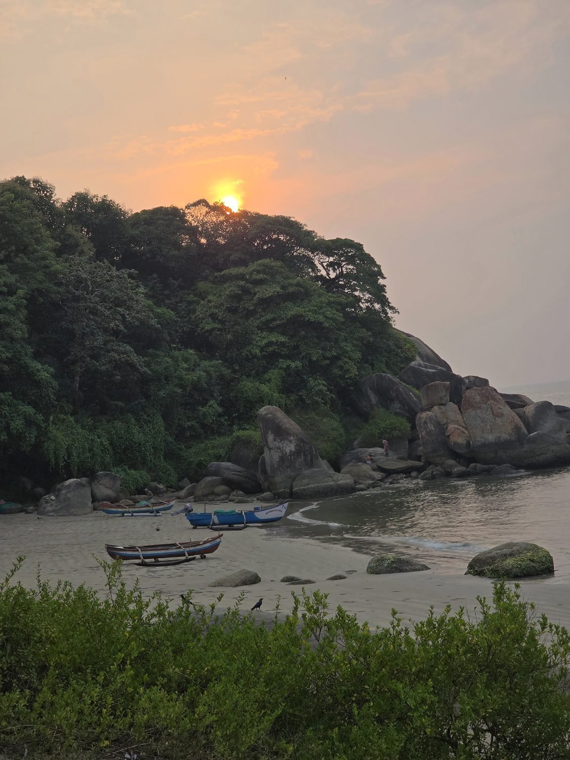 Sunset over rocky cove and fishing boats on the sand in Goa
